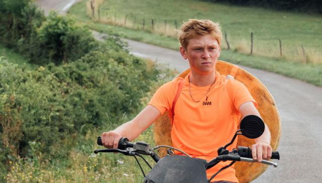 Photogramme du film montrant le protagoniste sur sa moto, une meule de comté accrochée au dos.